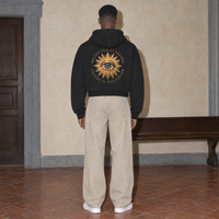 Man seen from behind wearing the black Believing full zip hoodie by Serenos, golden eye back print reading believing is seeing, cropped boxy fit