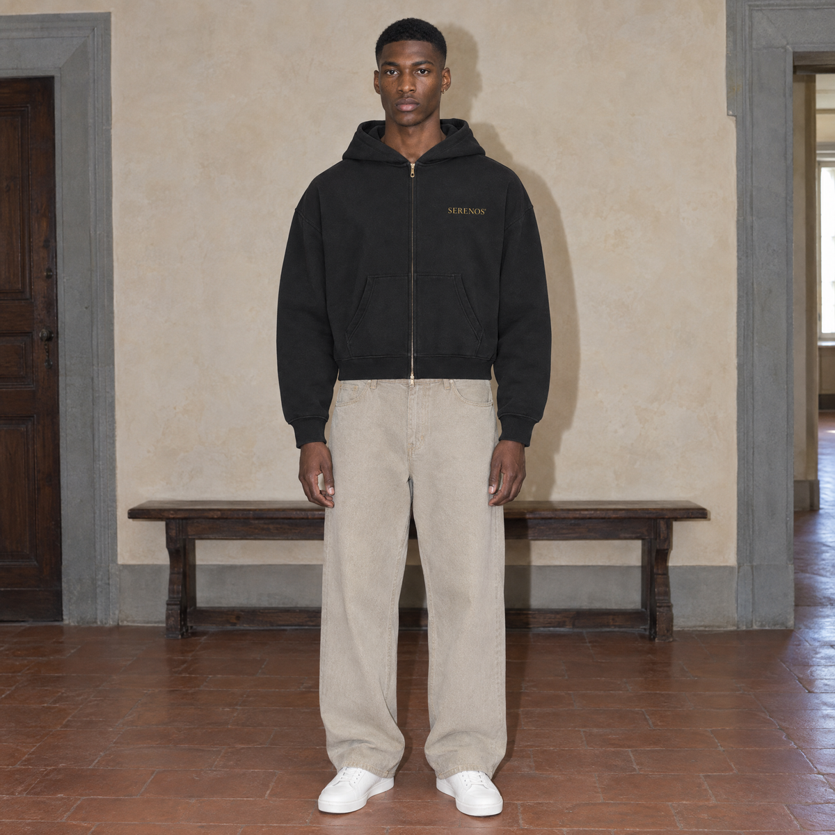 Man wearing the black Believing full zip hoodie by Serenos, front view with the gold Serenos chest logo, cropped boxy fit