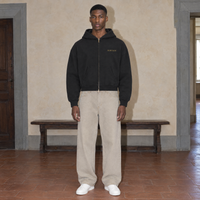 Man wearing the black Believing full zip hoodie by Serenos, front view with the gold Serenos chest logo, cropped boxy fit