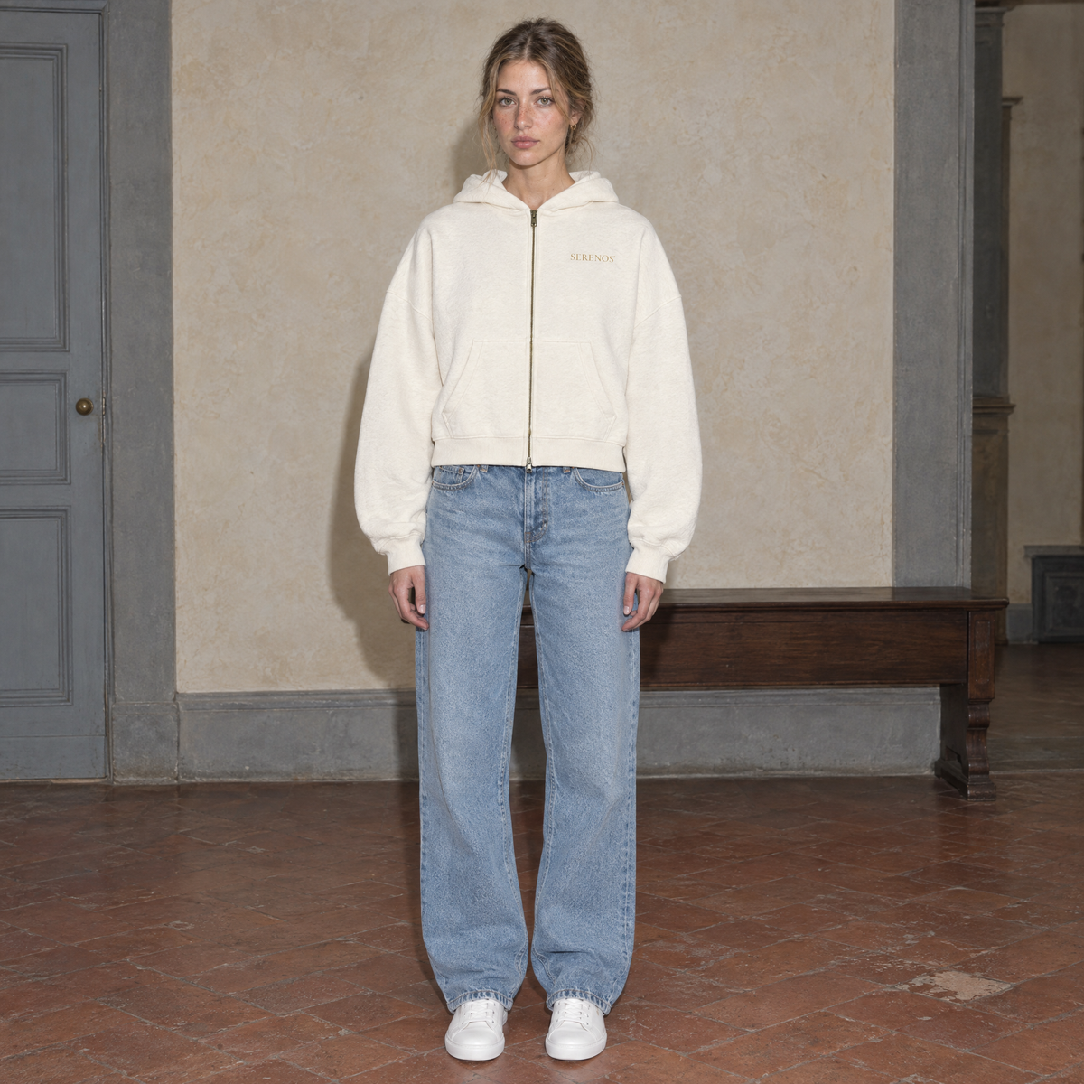 Woman wearing the cream Believing full zip hoodie by Serenos, front view with the gold Serenos chest logo, cropped boxy fit