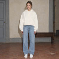 Woman wearing the cream Believing full zip hoodie by Serenos, front view with the gold Serenos chest logo, cropped boxy fit