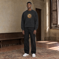 Man wearing the SERENOS Believing long sleeve in washed black, chest print of a golden sunburst eye circled by the words Believing is seeing