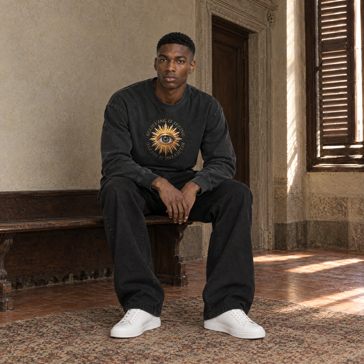 Man sitting on a bench in a Florentine palazzo wearing the SERENOS Believing long sleeve in washed black