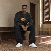 Man sitting on a bench in a Florentine palazzo wearing the SERENOS Believing long sleeve in washed black