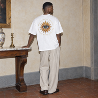 Man seen from behind wearing the white Believing oversized t-shirt by Serenos, golden eye back print reading believing is seeing
