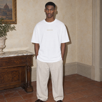Man wearing the white Believing oversized t-shirt by Serenos, front view with the small gold Serenos chest logo