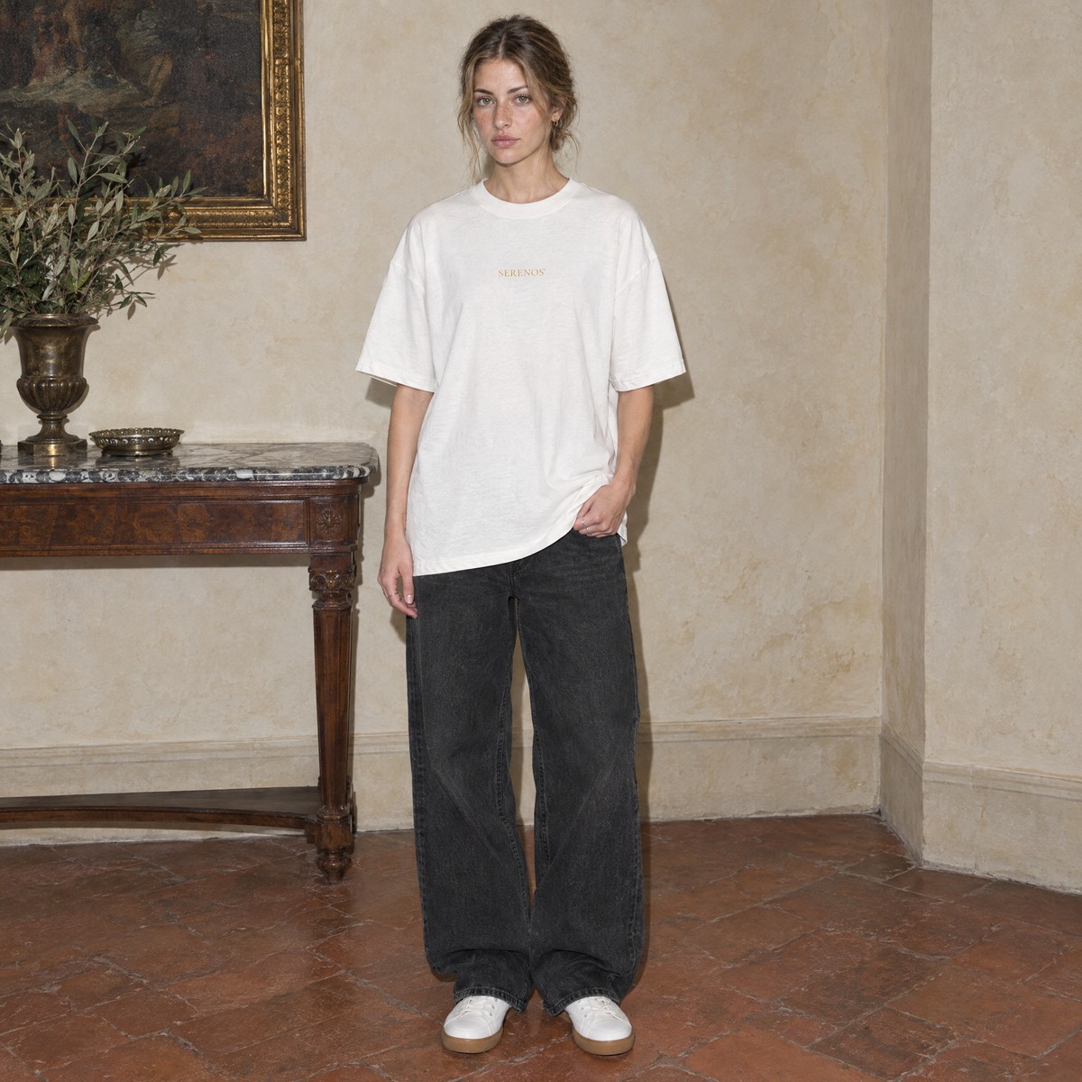 Woman wearing the white Believing oversized t-shirt by Serenos, front view with the small gold Serenos chest logo