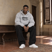 Man sitting on a bench in a Florentine palazzo wearing the SERENOS Best Day oversized boxy hoodie in flower gray