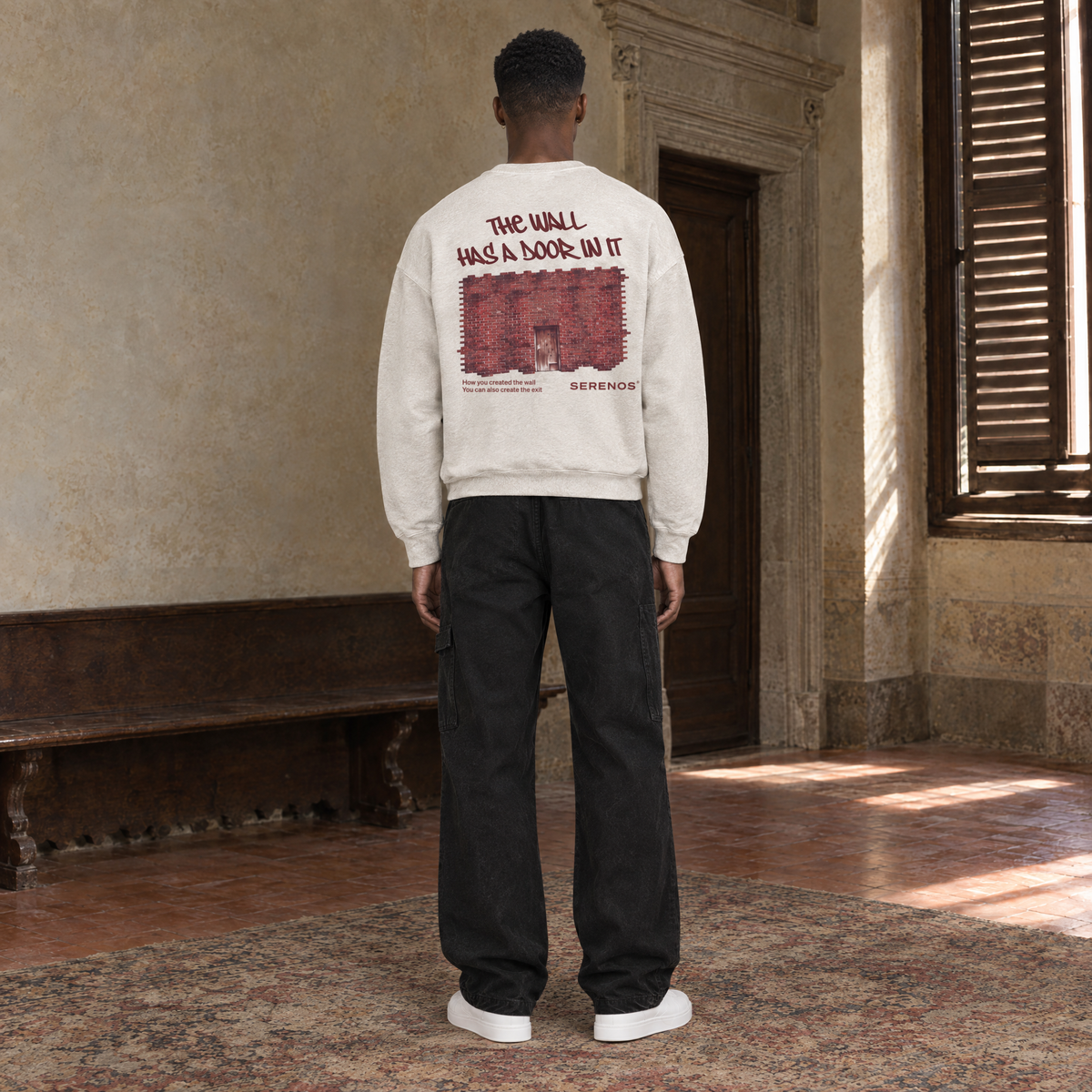 Man seen from behind wearing the SERENOS Door long sleeve in apricot, back print reading The wall has a door in it over a brick wall illustration