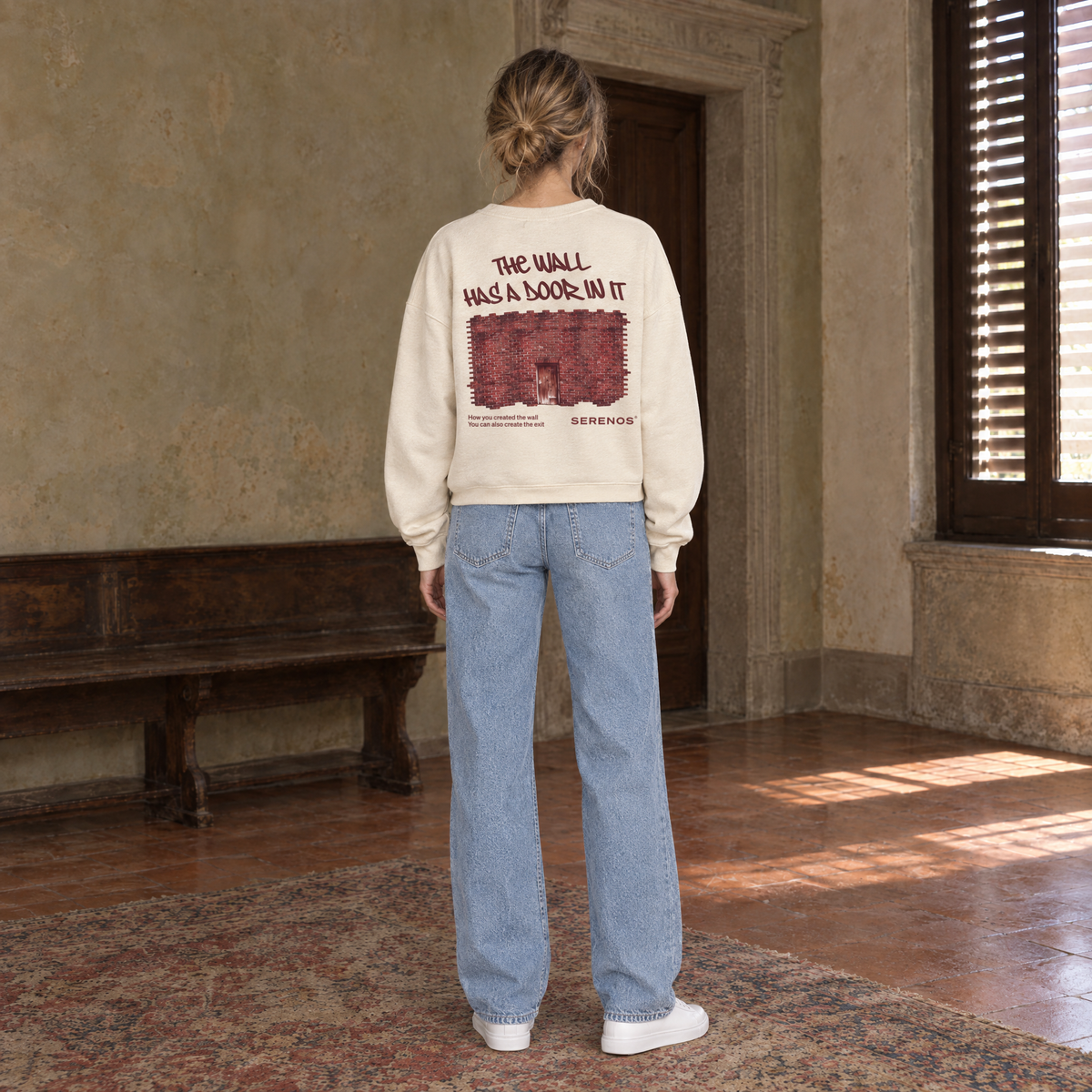 Woman seen from behind wearing the SERENOS Door long sleeve in apricot, back print reading The wall has a door in it over a brick wall illustration
