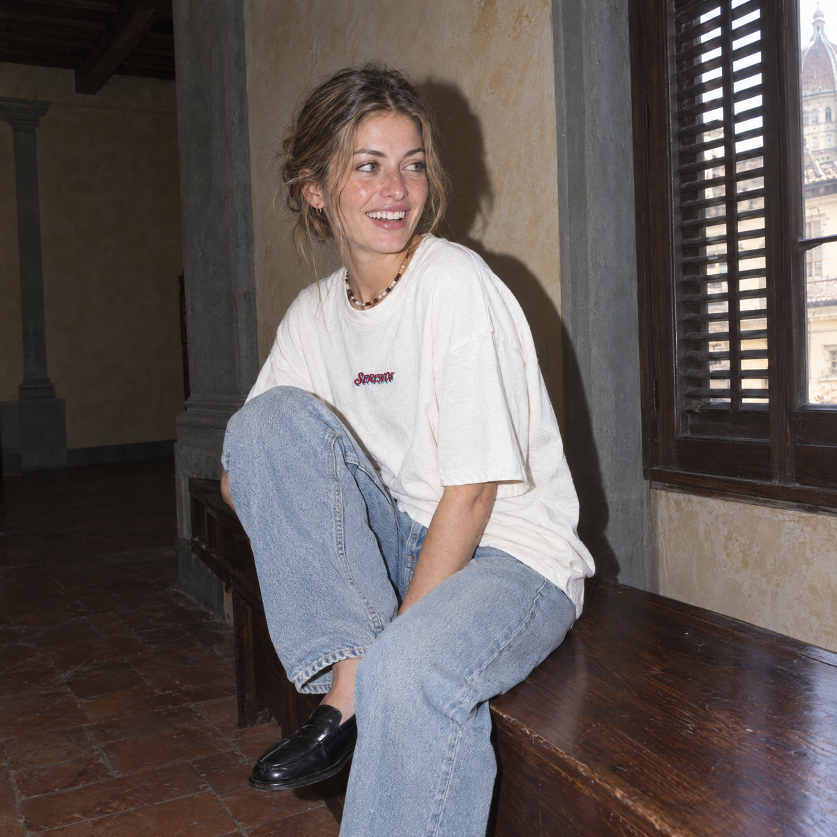 Lifestyle portrait of a woman in the SERENOS Final Version T-Shirt in white inside a Florentine palazzo