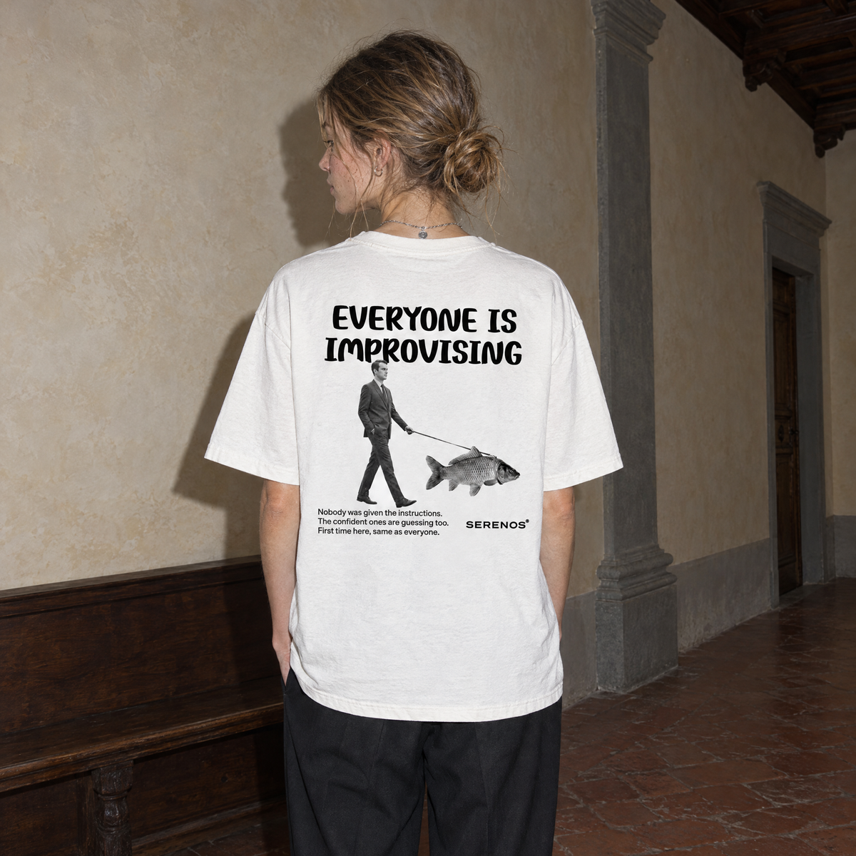 Woman wearing the white Improvising t-shirt from behind, back print reading Everyone is improvising with a man walking a fish on a leash