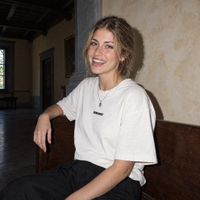 Woman laughing on a walnut bench in a Florentine palazzo wearing the white Improvising t-shirt