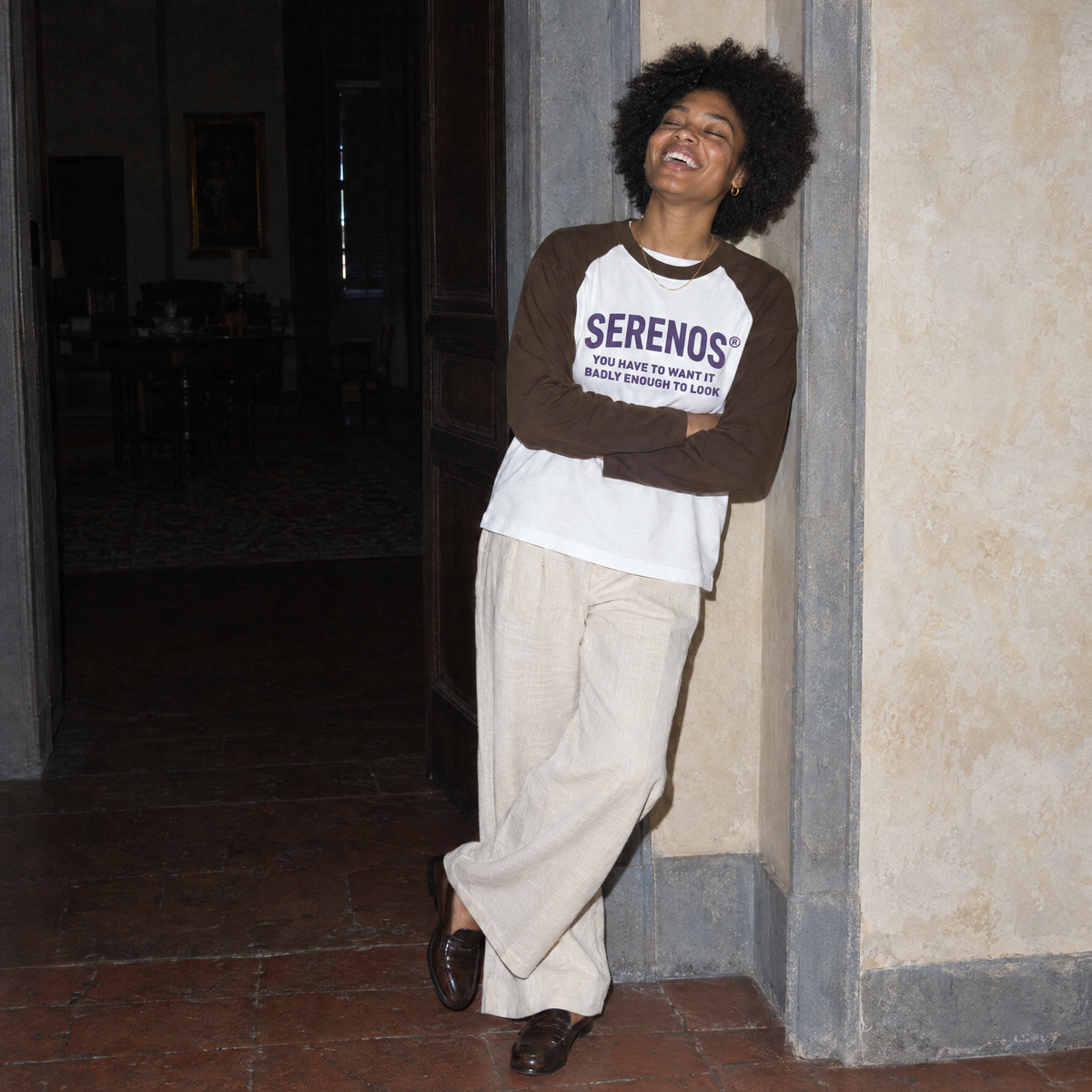 Woman laughing in a doorway of a Florentine palazzo wearing the Look raglan long sleeve by Serenos