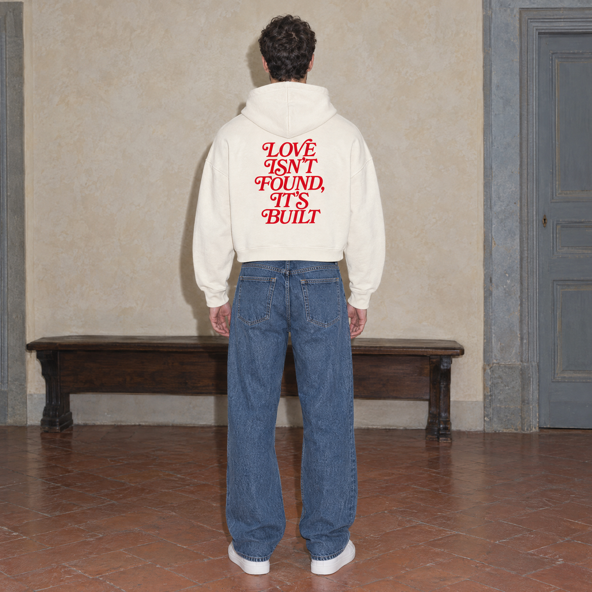 Man wearing the SERENOS Love Full Zip Hoodie in apricot, back print reading Love isn't found it's built, cropped boxy fit