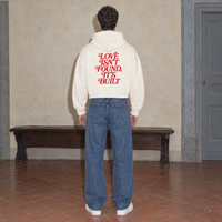Man wearing the SERENOS Love Full Zip Hoodie in apricot, back print reading Love isn't found it's built, cropped boxy fit