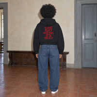 Woman wearing the SERENOS Love Full Zip Hoodie in black, back print reading Love isn't found it's built, cropped boxy fit