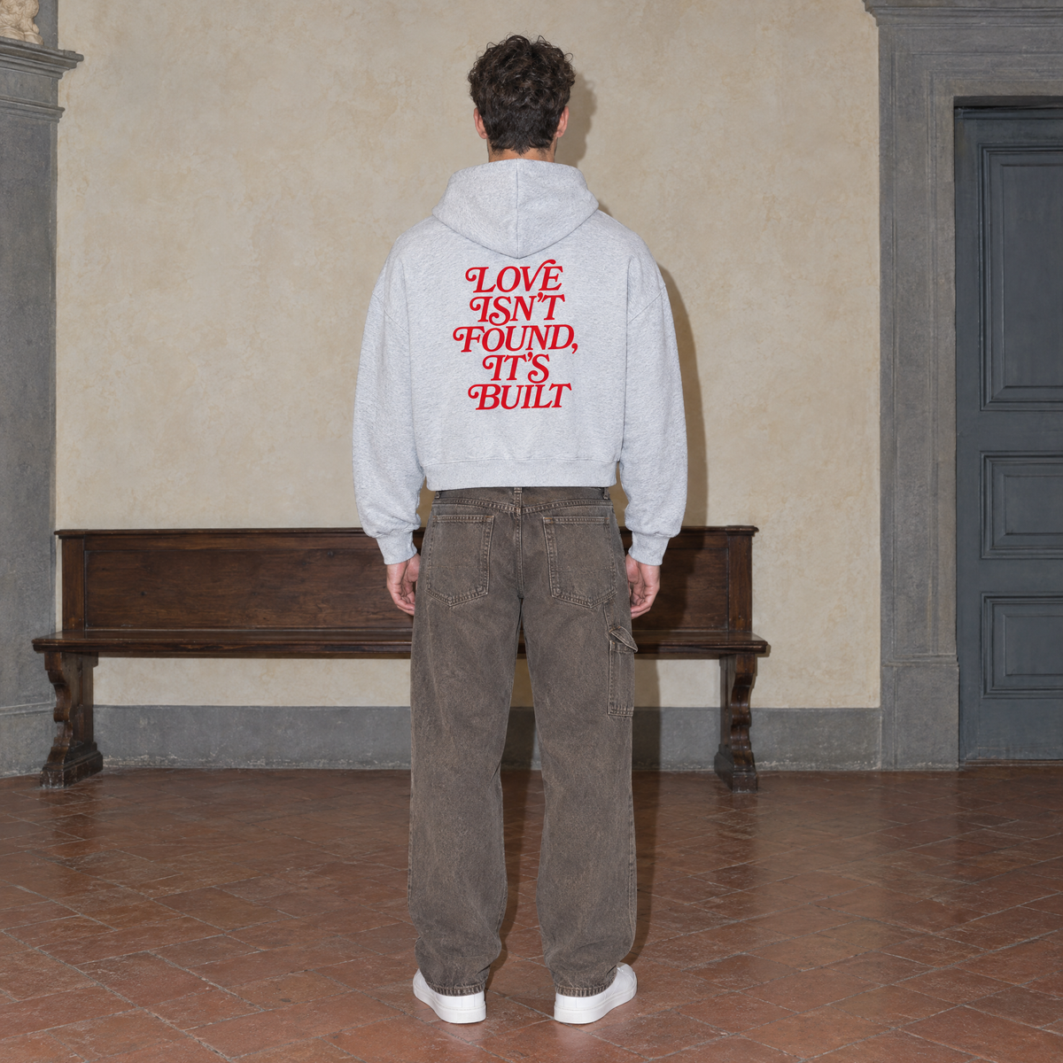 Man wearing the SERENOS Love Full Zip Hoodie in flower gray, back print reading Love isn't found it's built, cropped boxy fit