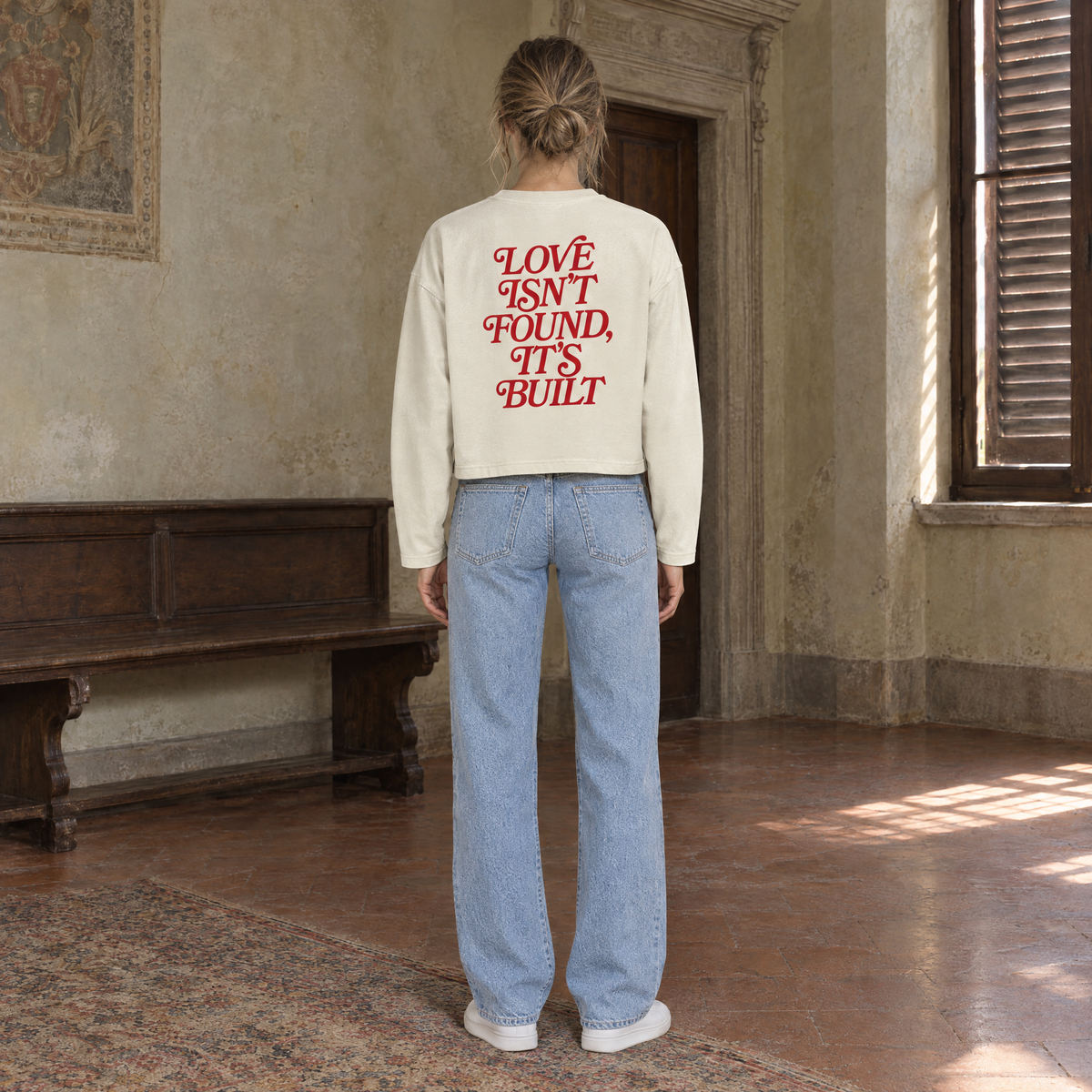 Woman seen from behind wearing the SERENOS Love long sleeve in apricot, back print in red serif reading Love isn't found, it's built