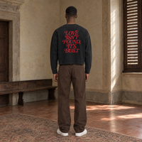 Man seen from behind wearing the SERENOS Love long sleeve in black, back print in red serif reading Love isn't found, it's built