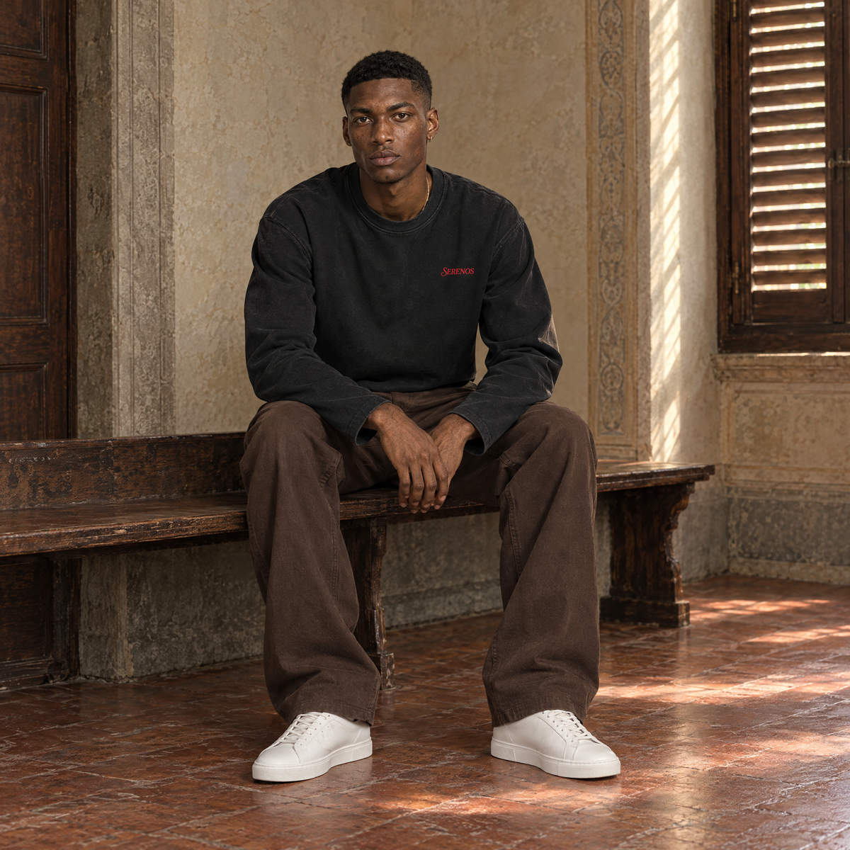 Man sitting on a bench in a Florentine palazzo wearing the SERENOS Love long sleeve in black