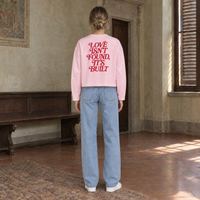 Woman seen from behind wearing the SERENOS Love long sleeve in pink, back print in red serif reading Love isn't found, it's built