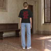 Woman seen from behind wearing the SERENOS Love T-Shirt in black, back print in red serif reading Love isn't found, it's built