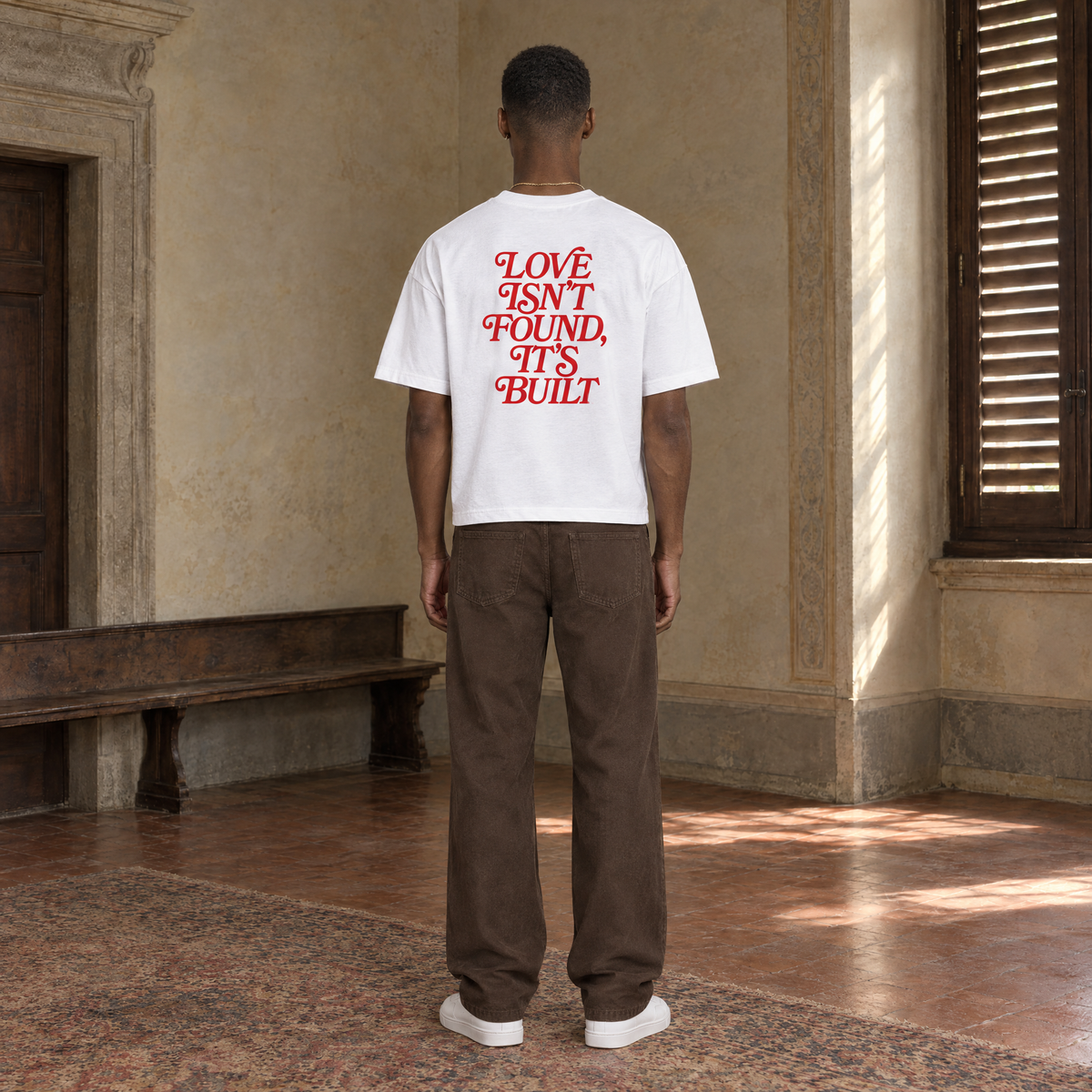 Man seen from behind wearing the SERENOS Love T-Shirt in white, back print in red serif reading Love isn't found, it's built
