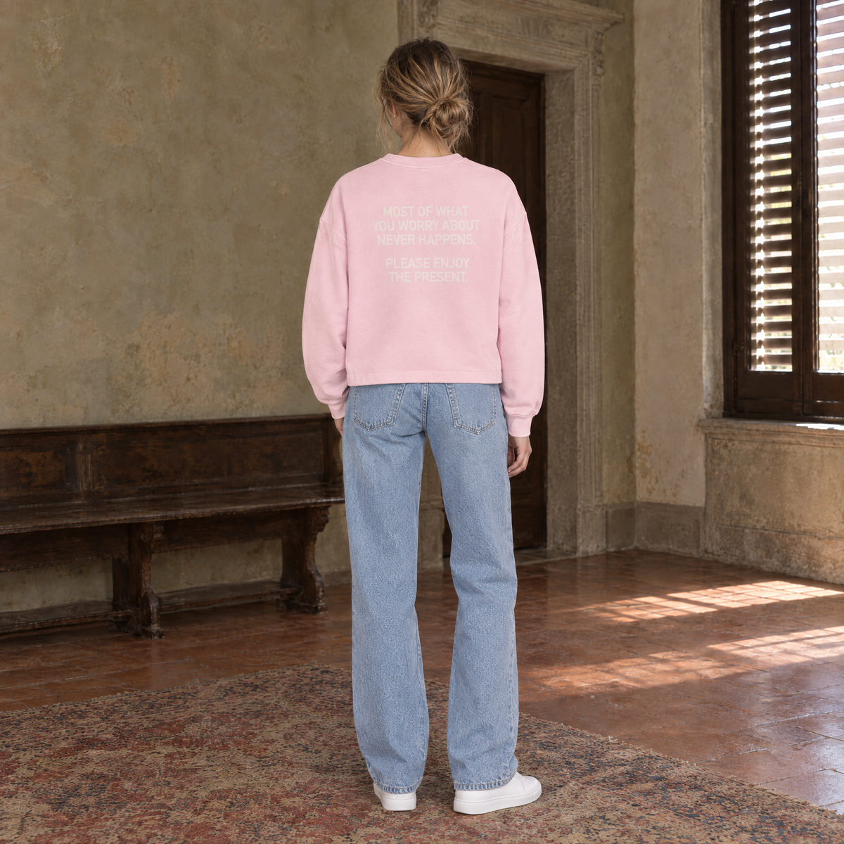 Woman seen from behind wearing the SERENOS Never Happens long sleeve in pink, back print reading Most of what you worry about never happens, please enjoy the present
