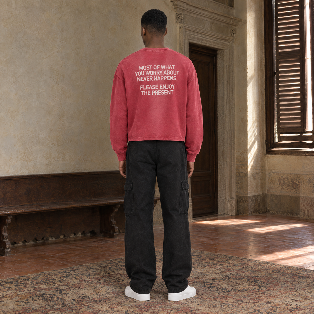 Man seen from behind wearing the SERENOS Never Happens long sleeve in red, back print reading Most of what you worry about never happens, please enjoy the present