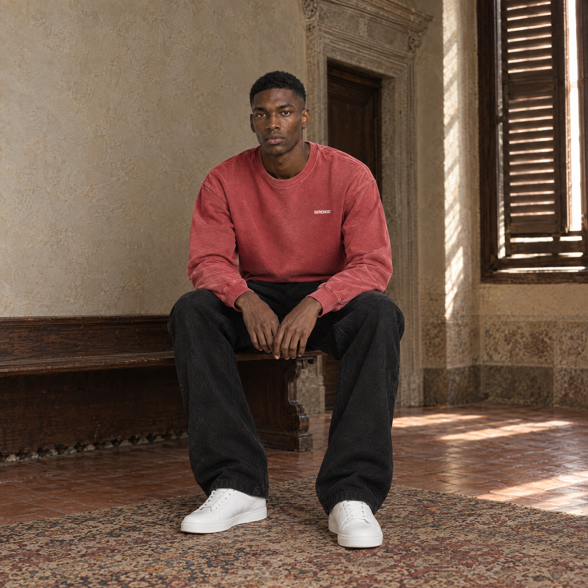 Man sitting on a bench in a Florentine palazzo wearing the SERENOS Never Happens long sleeve in red