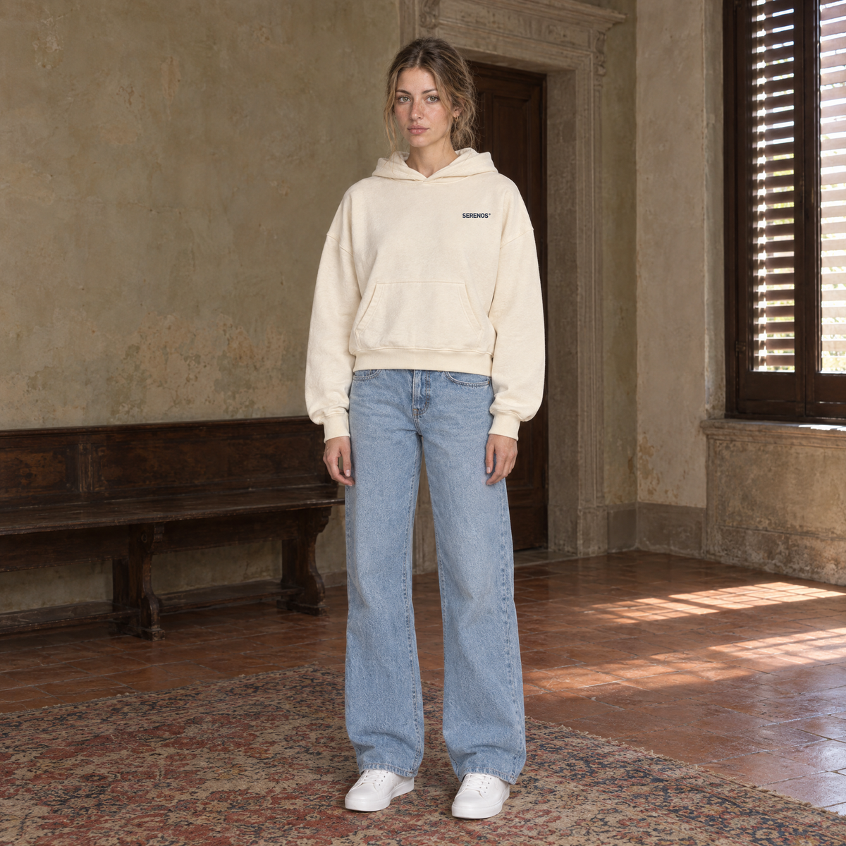 Woman wearing the SERENOS Never Happens oversized boxy hoodie in apricot, front view with the small navy chest logo, cropped boxy fit