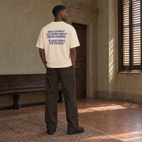 Man wearing the SERENOS Never Happens T-Shirt in apricot, back print reading Most of what you worry about never happens, please enjoy the present