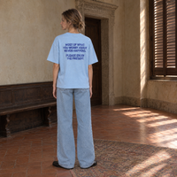 Woman wearing the SERENOS Never Happens T-Shirt in blue, back print reading Most of what you worry about never happens, please enjoy the present