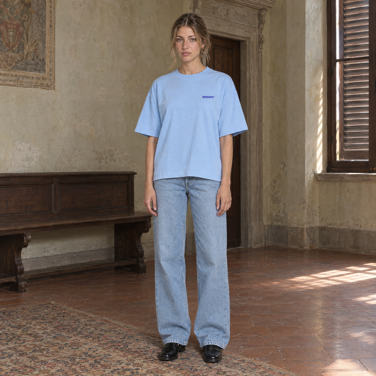 Woman wearing the SERENOS Never Happens T-Shirt in blue, front view with the small blue chest logo