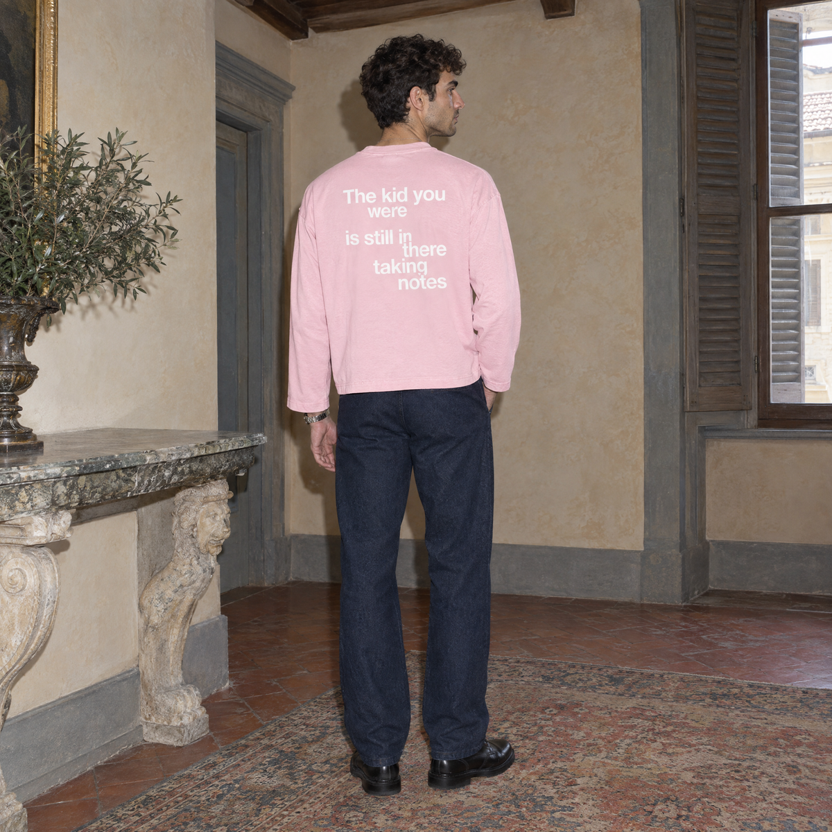 Man wearing the SERENOS Notes Long Sleeve in pink, back print reading The kid you were is still in there taking notes