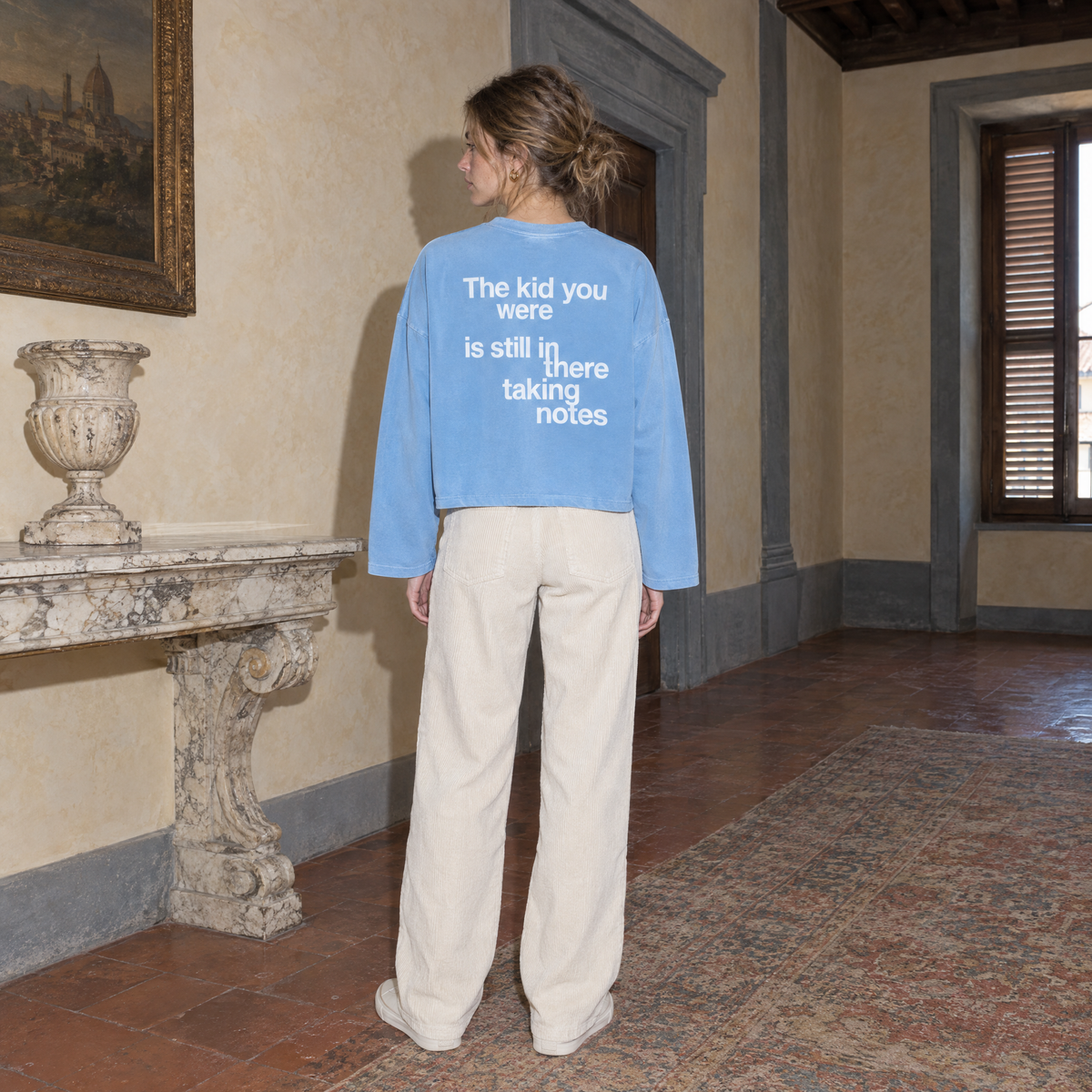 Woman wearing the SERENOS Notes Long Sleeve in sky blue, back print reading The kid you were is still in there taking notes