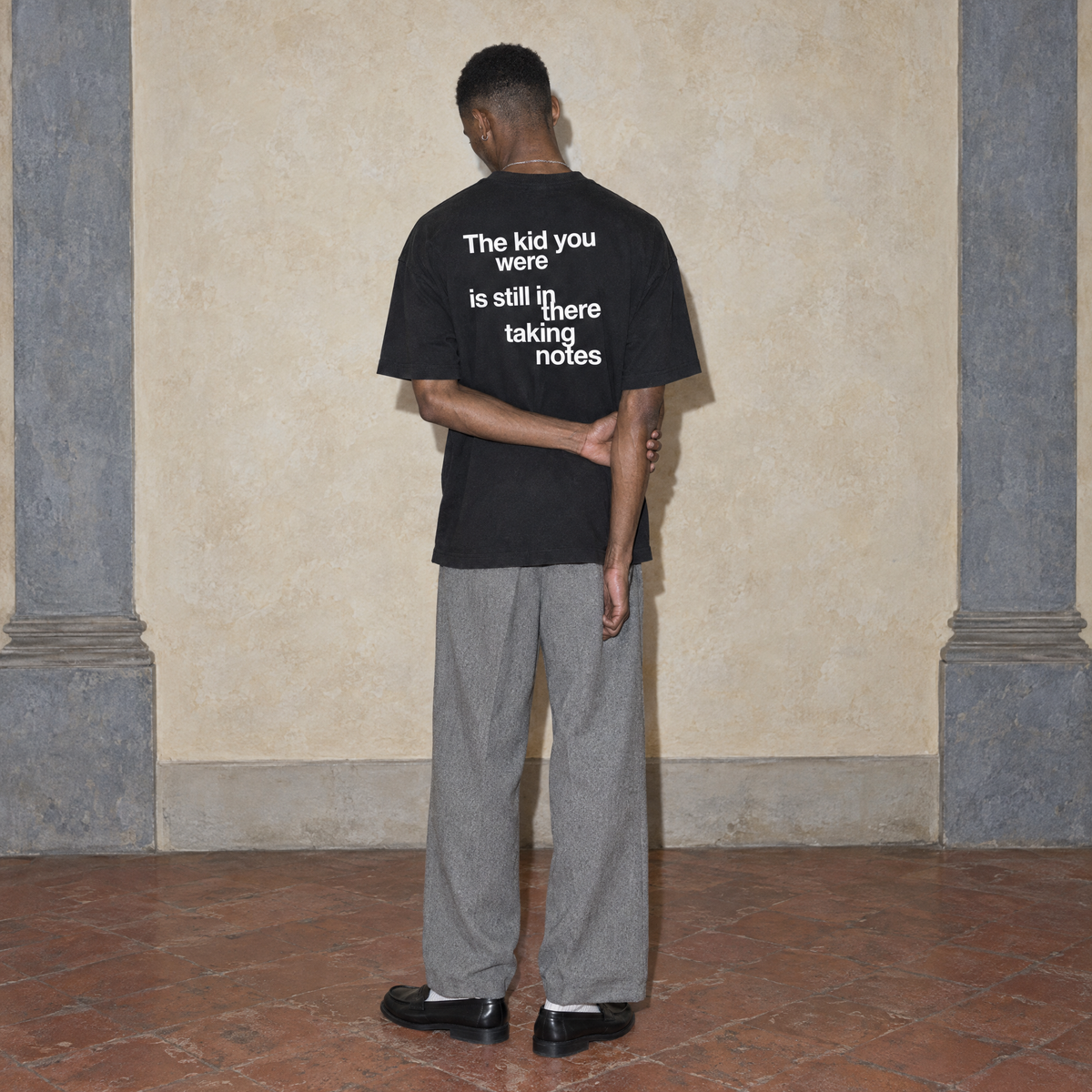 Man seen from behind wearing the black Notes oversized t-shirt by Serenos, back print reading the kid you were is still in there taking notes