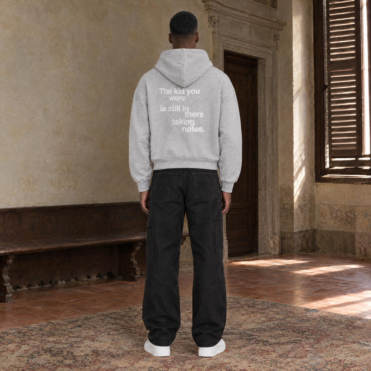 Man seen from behind wearing the SERENOS Notes zip hoodie in flower gray, back print reading The kid you were is still in there taking notes, cropped boxy fit