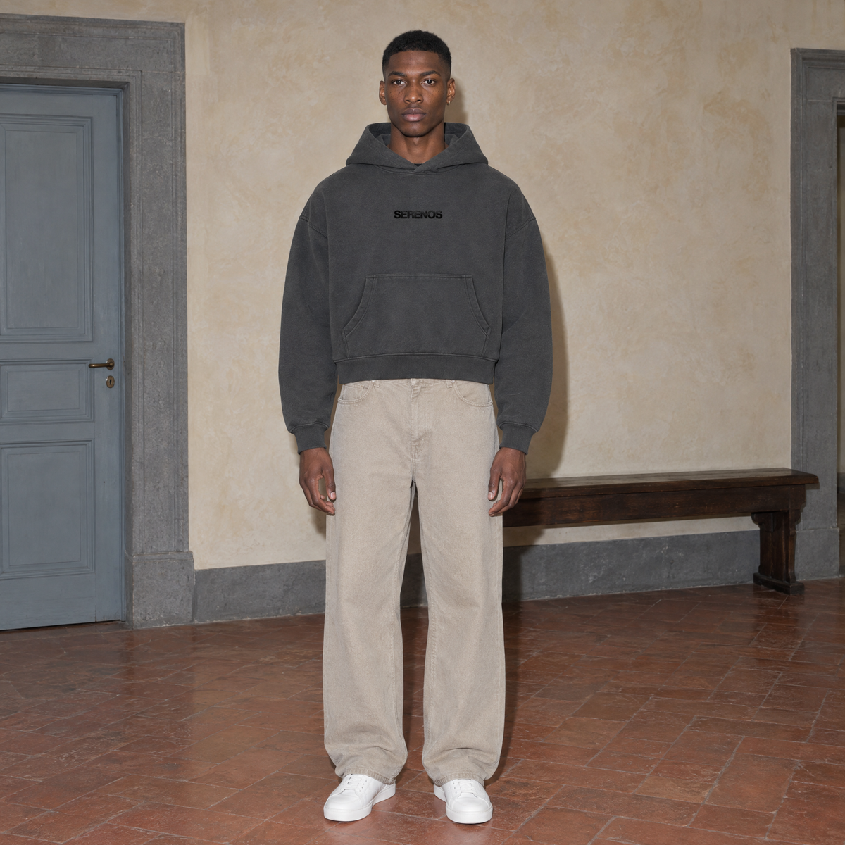 Man wearing the SERENOS Organizes oversized boxy hoodie in dark gray, front view with the centred SERENOS chest logo, cropped boxy fit