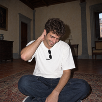 Man laughing while sitting on a rug in a Florentine palazzo wearing the white Organizes t-shirt