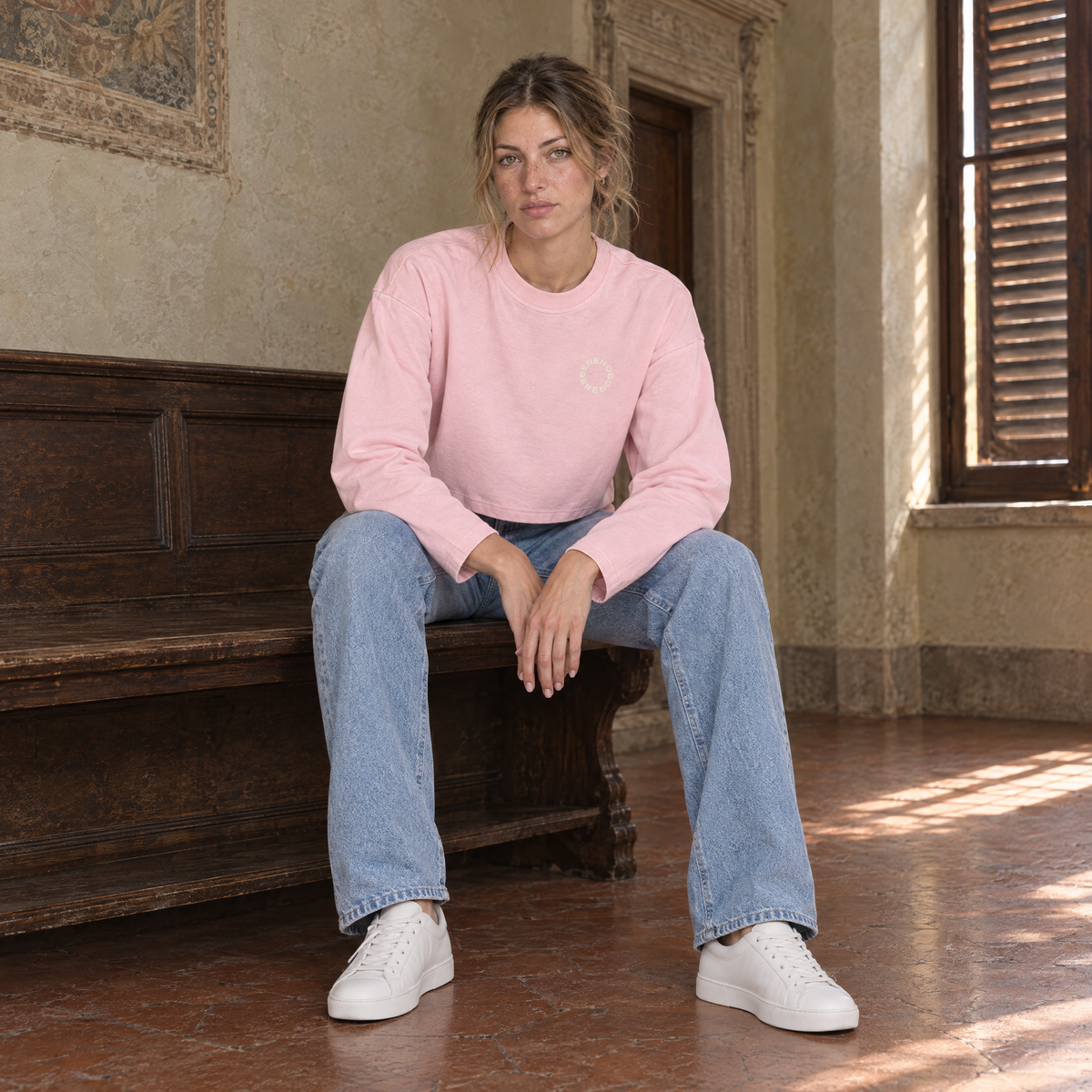 Woman sitting on a bench in a Florentine palazzo wearing the SERENOS Shy long sleeve in pink