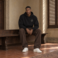 Man sitting on a bench in a Florentine palazzo wearing the SERENOS Shy oversized boxy hoodie in black