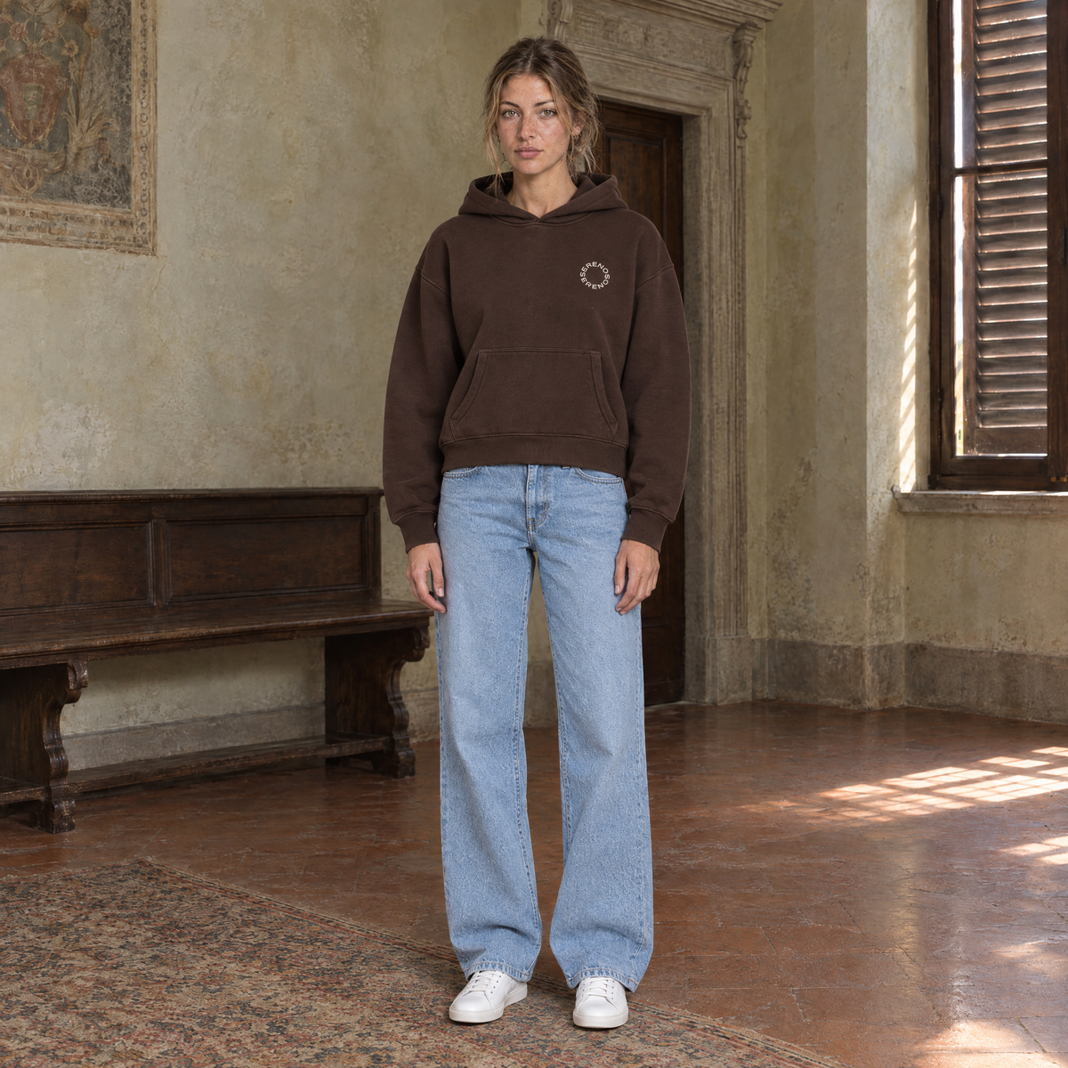 Woman wearing the SERENOS Shy oversized boxy hoodie in coffee, front view with the small ring logo on the chest