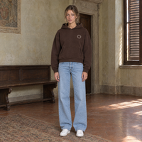 Woman wearing the SERENOS Shy oversized boxy hoodie in coffee, front view with the small ring logo on the chest