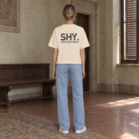 Woman seen from behind wearing the SERENOS Shy T-Shirt in apricot, back print reading Shy, talk to me anyway