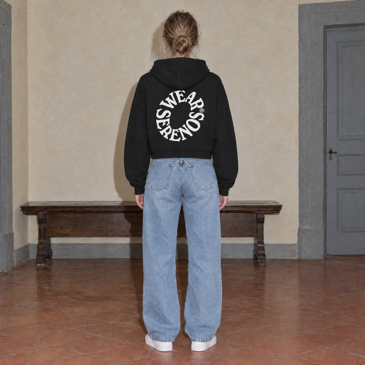 Woman seen from behind wearing the SERENOS Spiral oversized boxy hoodie in black, back print of Wear Serenos set around a circle