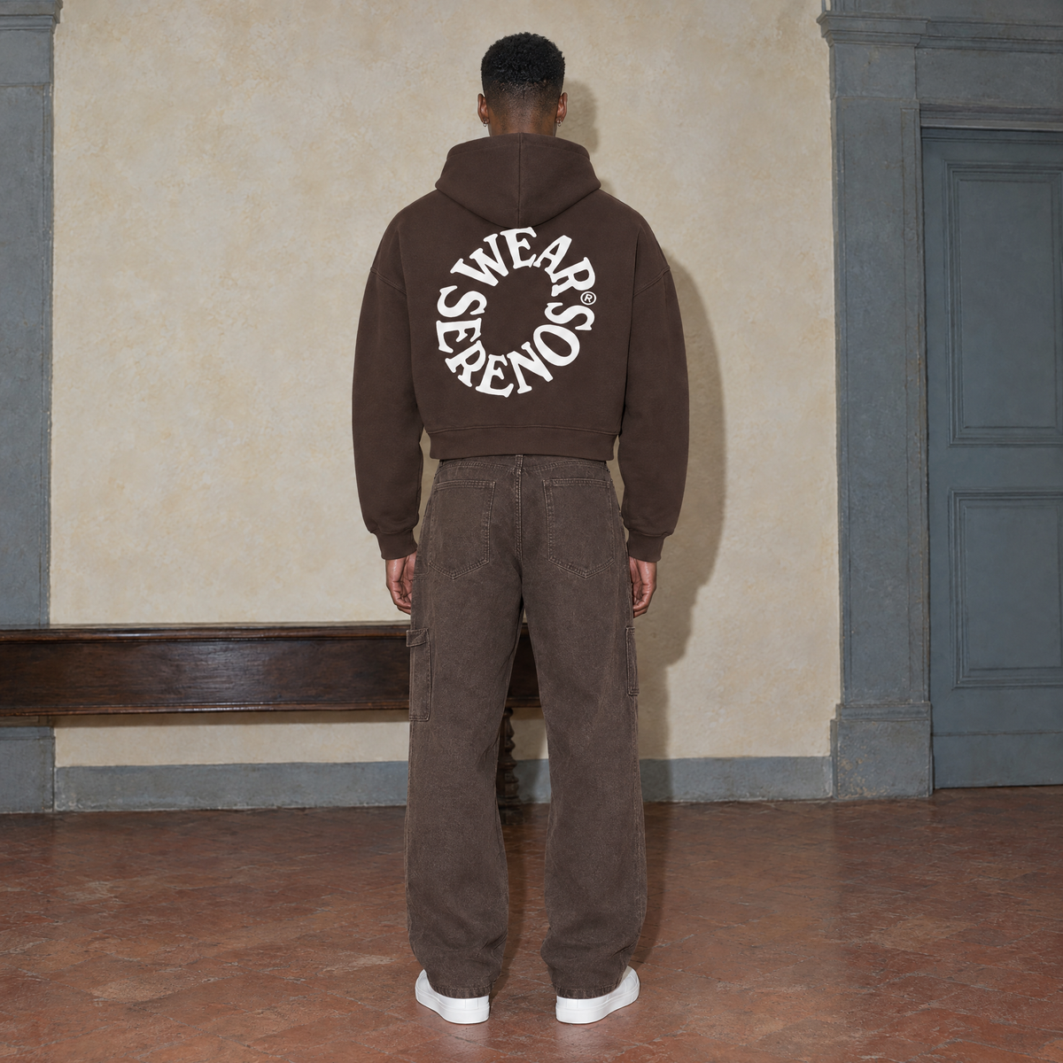 Man seen from behind wearing the SERENOS Spiral oversized boxy hoodie in coffee, back print of Wear Serenos set around a circle