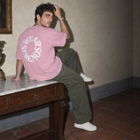 Man sitting on a marble console in a Florentine palazzo wearing the pink Spiral oversized t-shirt by Serenos