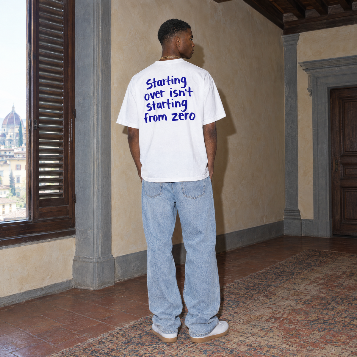 Man wearing the white Start Over t-shirt from behind, blue brush-lettered back print reading Starting over isn't starting from zero